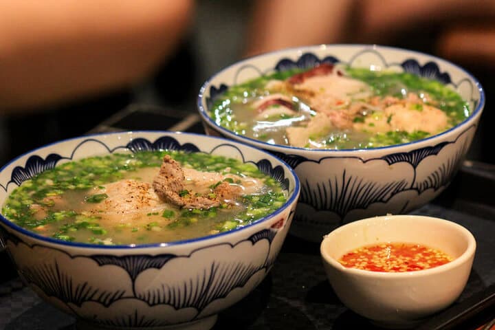 Hai tô bún quậy nước dùng nhạt màu, chả và hành, bên cạnh có chén nước chấm