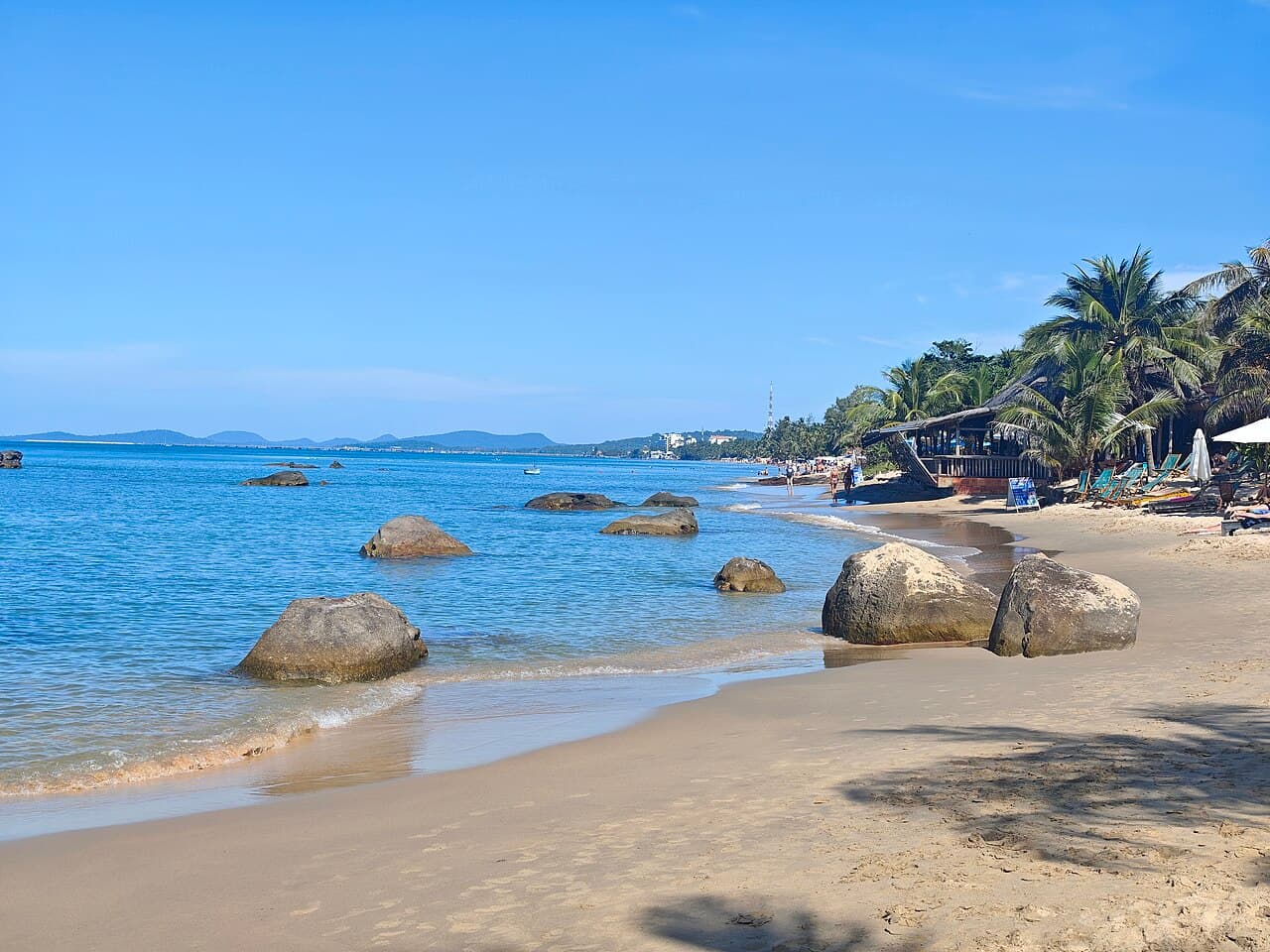 Đá tròn trên bờ cát, phía sau là hàng dừa và chỗ nghỉ ven biển