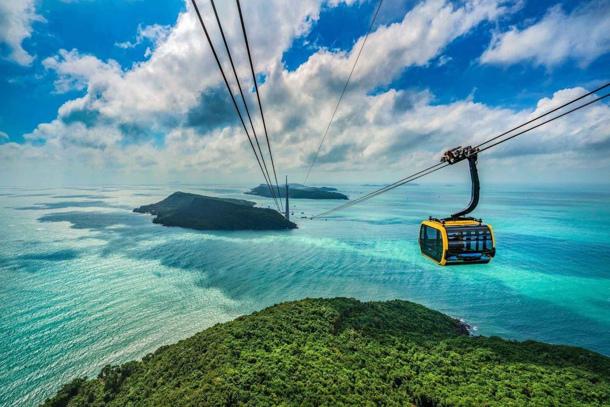 Cabin cáp treo màu vàng đen treo trên dây cáp, phía dưới là biển xanh ngọc, các hòn đảo nhỏ và một trụ cáp