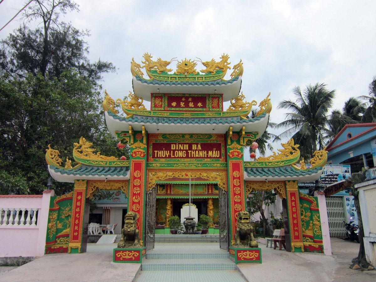 Cổng tam quan sơn đỏ, xanh và vàng, hai tượng lân đứng hai bên bậc thềm, qua khung cổng thấy lư hương và chánh điện.