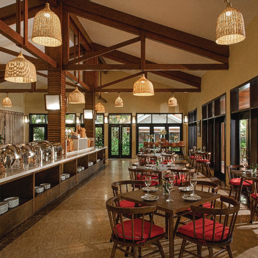 Phòng ăn mái gỗ với đèn mây treo, quầy buffet dọc tường và các bàn ghế đệm đỏ.