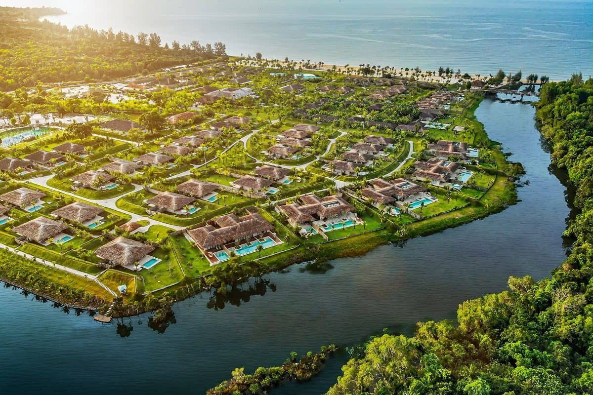 Ảnh chụp từ trên cao các biệt thự mái lá giữa vườn cây, một bên là nhánh sông, xa xa là biển