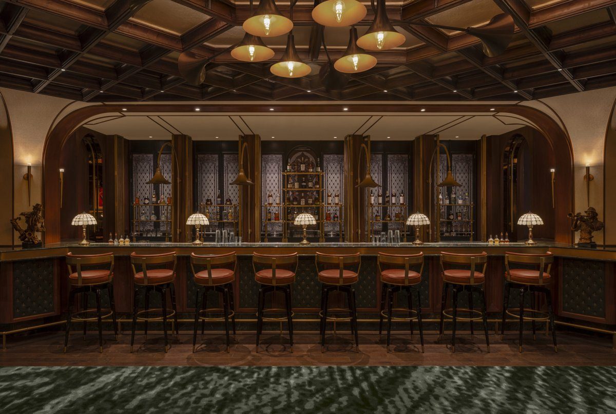 Quầy bar dài với tám ghế cao bọc da nâu đỏ, đèn bàn chao kính màu, kệ rượu phía sau, hai tượng đồng nhỏ ở hai đầu quầy