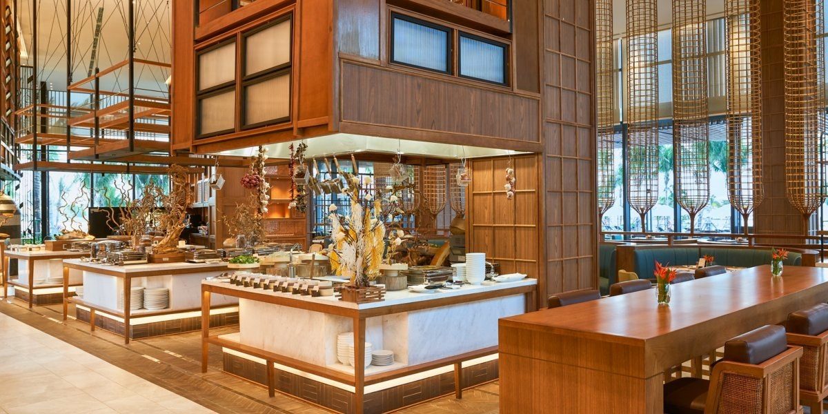Không gian nhà hàng với quầy buffet, bếp mở, nội thất gỗ và cửa kính lớn.