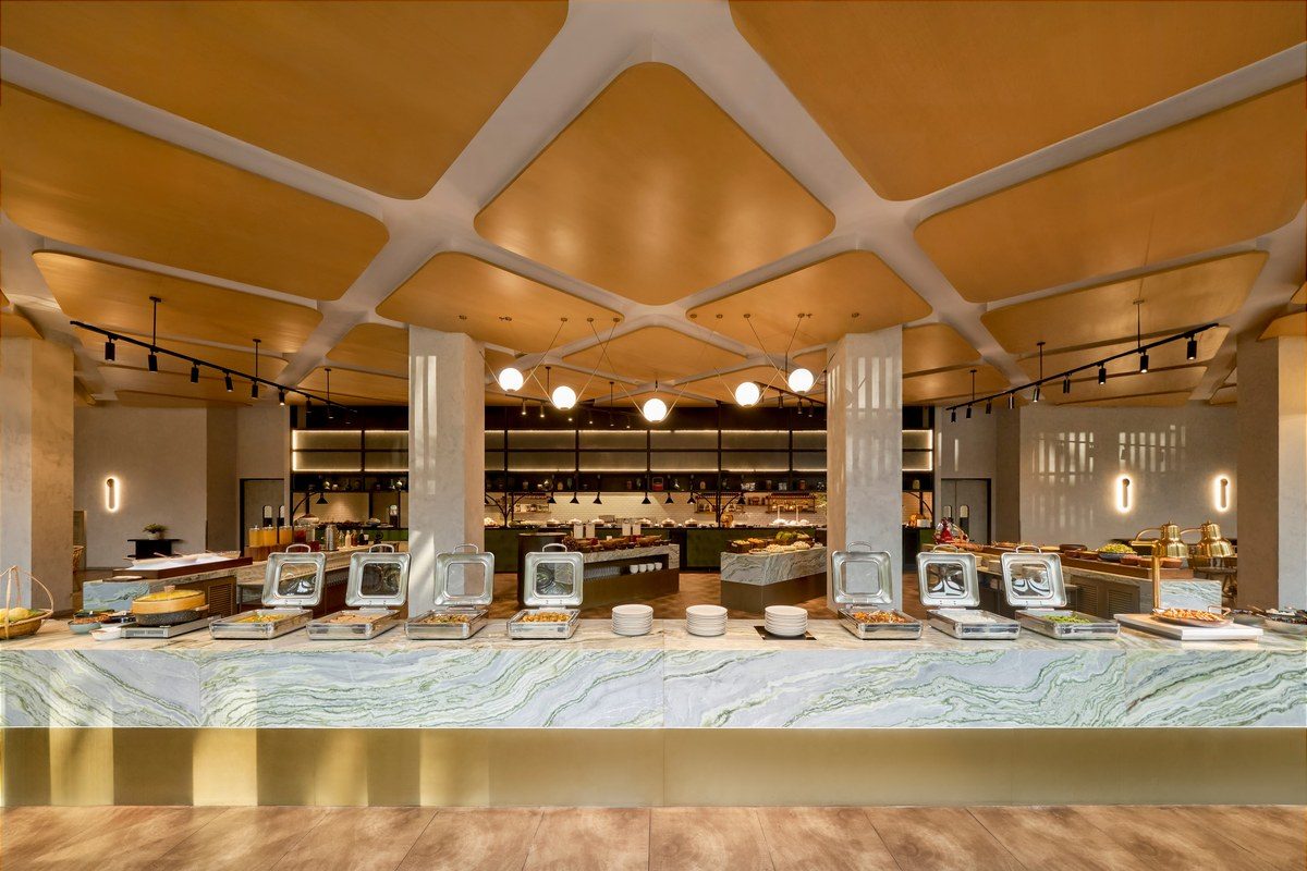 Dãy quầy buffet bằng đá vân xanh dưới trần gỗ lượn sóng.