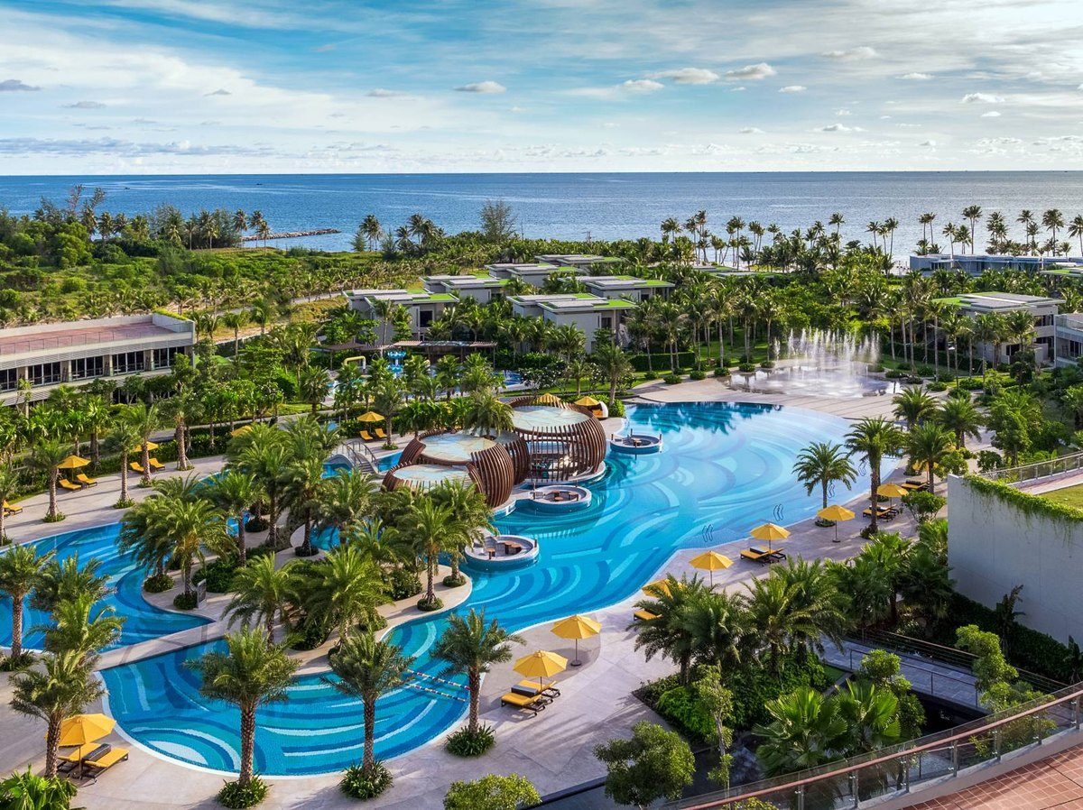 Toàn cảnh Pullman Phú Quốc nhìn từ trên cao: hồ bơi xanh uốn lượn, hàng dừa, các khối nhà thấp và biển phía xa