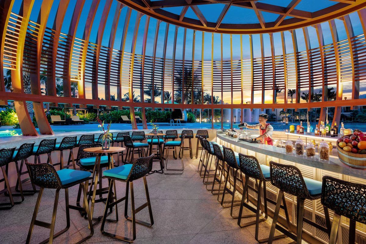 Quầy bar hình vòm bên hồ bơi, ghế cao xếp quanh quầy, trời chiều phía sau