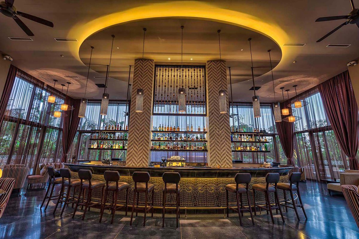 Quầy bar hình vòng cung với ghế cao, kệ rượu sáng đèn và trần đèn tròn màu vàng