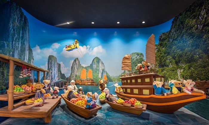 Mô hình vịnh Hạ Long với núi đá vôi, nhiều thuyền gỗ nhỏ chở trái cây do gấu bông chèo, một tàu buồm lớn và máy bay đồ chơi màu vàng trên trời