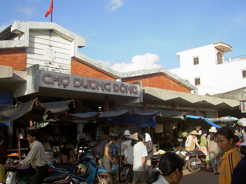 Ворота рынка с вывеской Chợ Dương Đông, перед ними люди и мотобайки